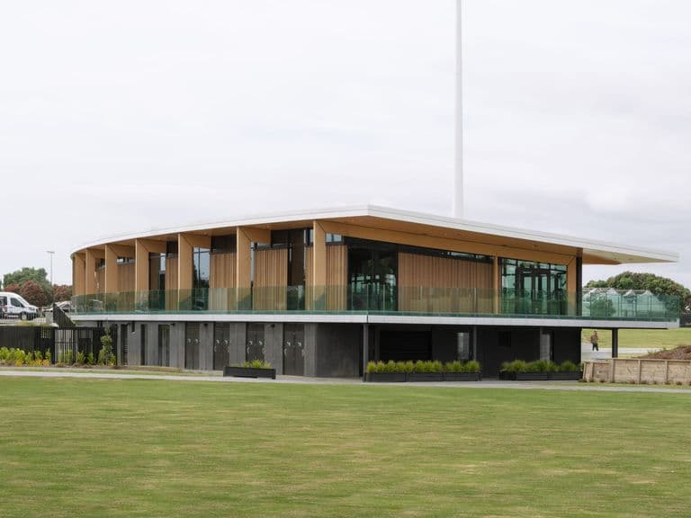 Completed two-storey pavilion with timber-clad upper level and a glazed balcony overlooking a playing field