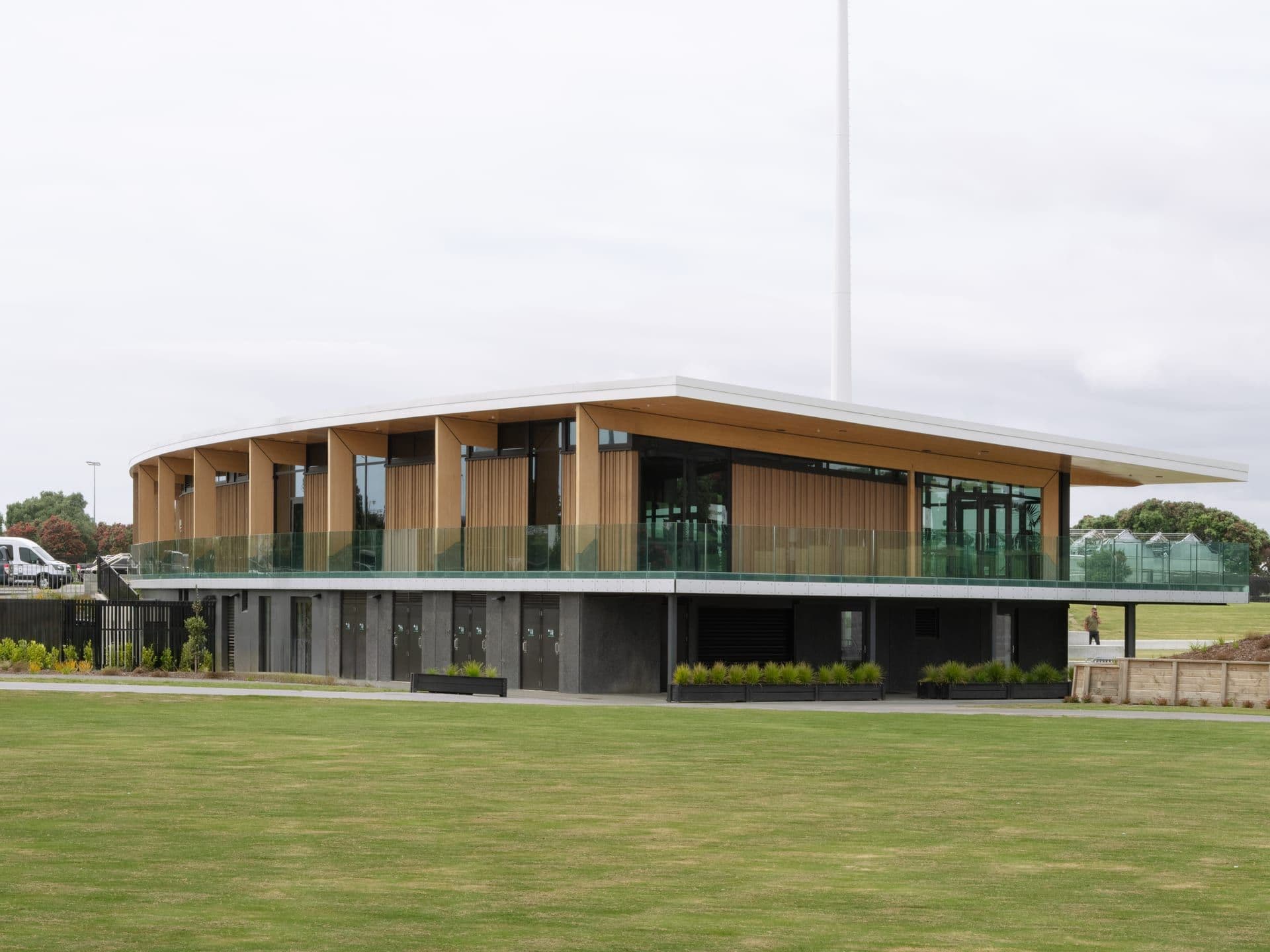 Completed two-storey pavilion with timber-clad upper level and a glazed balcony overlooking a playing field